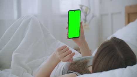 Young-woman-lying-in-bed-making-a-video-call-to-the-doctor-looking-at-the-green-screen-of-the-chromakey